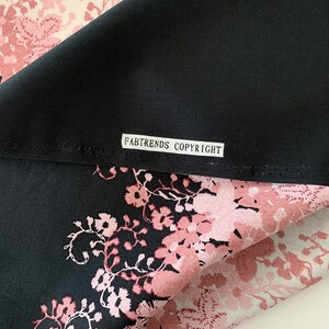 May include: Black fabric with a pink floral print. The fabric has a label that reads "FABTRENDS COPYRIGHT".