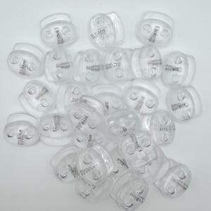 May include: A collection of clear plastic cord locks, designed for securing drawstrings or cords. Each lock features a spring mechanism and two holes for cord insertion. The transparent material allows for easy visibility of the cord.