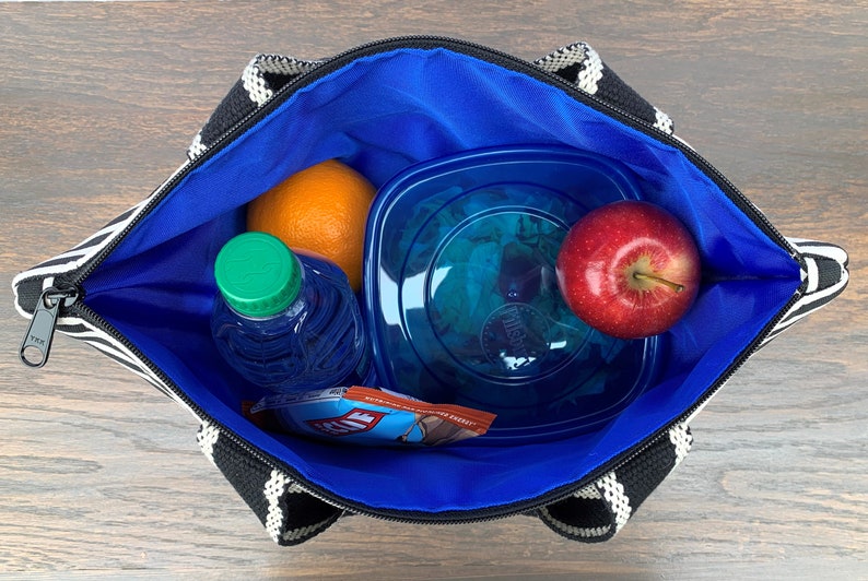 May include: A black and white striped lunch bag with a blue lining. The bag is open and contains a blue water bottle, an orange, a blue plastic container with a green salad, and a red apple.