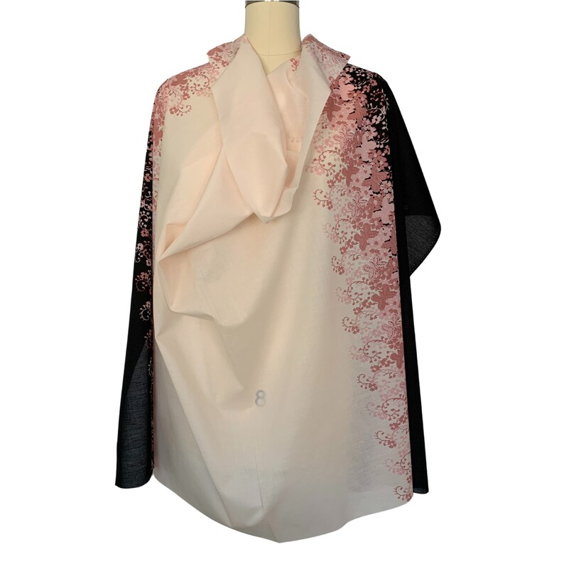 May include: A white and black patterned blouse with a draped neckline. The blouse has a pink floral print on one side and a black fabric on the other side.