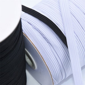 May include: Close-up of spools of elastic ribbon in black and white. The white ribbon is a light blue color. The elastic is tightly wound on cardboard spools. The elastic is used for sewing and crafting.