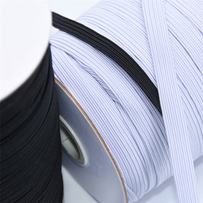 May include: Close-up of spools of elastic ribbon in black and white. The white ribbon is a light blue color. The elastic is tightly wound on cardboard spools. The elastic is used for sewing and crafting.
