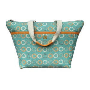 May include: A teal blue tote bag with orange and white circle pattern. The bag has two cream colored handles and a zipper closure.