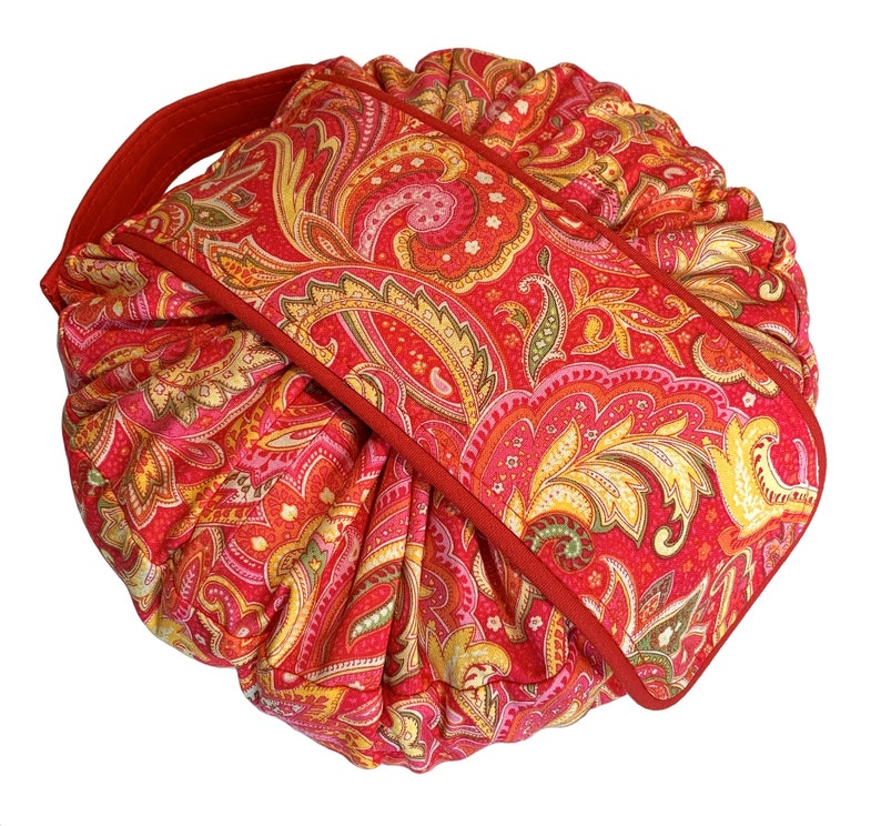 May include: Red paisley patterned drawstring bag with a red handle. The bag is folded and tied with a red ribbon.