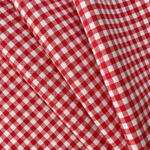 Può includere: Tessuto gingham rosso e bianco con un motivo a quadri. Il tessuto è piegato in tre, creando un effetto a strati.