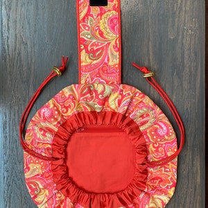 May include: A red drawstring bag with a paisley pattern and a zippered pocket. The bag has a handle with a velcro closure.