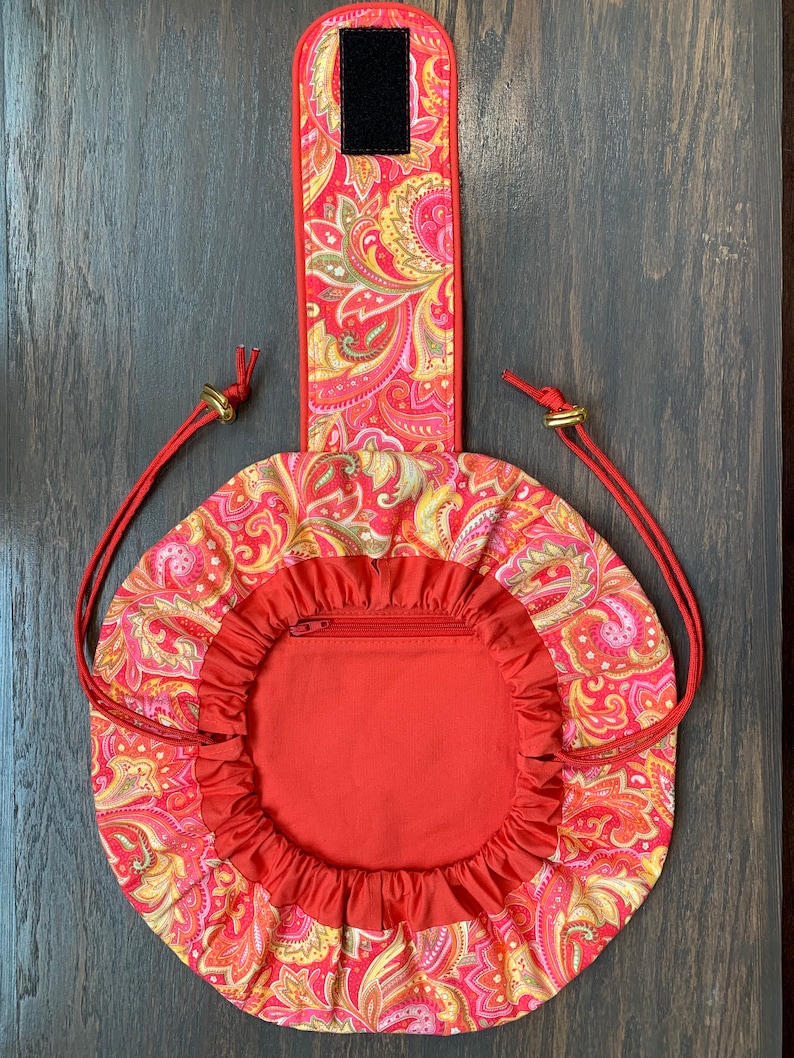 May include: A red drawstring bag with a paisley pattern and a zippered pocket. The bag has a handle with a velcro closure.