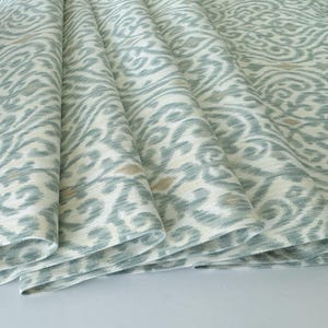 Könnte beinhalten: Nahaufnahme eines gefalteten Stoffes mit einem sich wiederholenden Muster in Blau-, Beige- und Weißtönen. Das Design weist wirbelnde, organische Formen auf, die ein strukturiertes Aussehen erzeugen. Der Stoff ist drapiert und zeigt die Falten und die Textur.