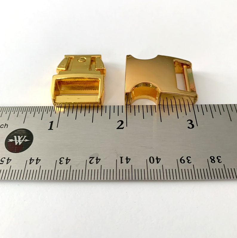 May include: Two gold-colored metal clasps for a dog collar or leash, measured against a ruler. The clasps are about 1 inch long.