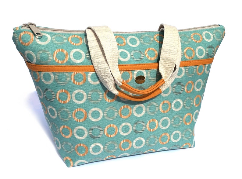 May include: A teal blue tote bag with white and orange circles. The bag has a zipper closure and two cream-colored handles.
