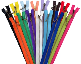 Könnte beinhalten: Eine Ansammlung von Reißverschlüssen, die fächerförmig angeordnet sind und eine Vielzahl leuchtender Farben wie Schwarz, Orange, Gelb, Grün, Lila, Weiß, Hellblau, Dunkelblau, Limettengrün und Pink aufweisen, jeweils mit einem bronzefarbenen Schieber.