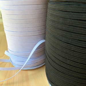 May include: Two spools of elastic ribbon, one light purple and the other dark brown. The elastic is tightly wound on cardboard spools. A length of white elastic ribbon is visible, extending from the light purple spool.