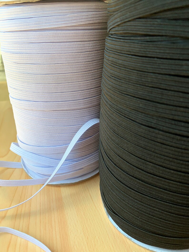 May include: Two spools of elastic ribbon, one light purple and the other dark brown. The elastic is tightly wound on cardboard spools. A length of white elastic ribbon is visible, extending from the light purple spool.