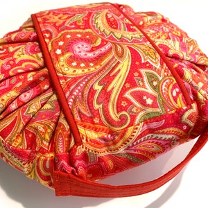 May include: A red, yellow, and green paisley patterned fabric pouch with a red handle.