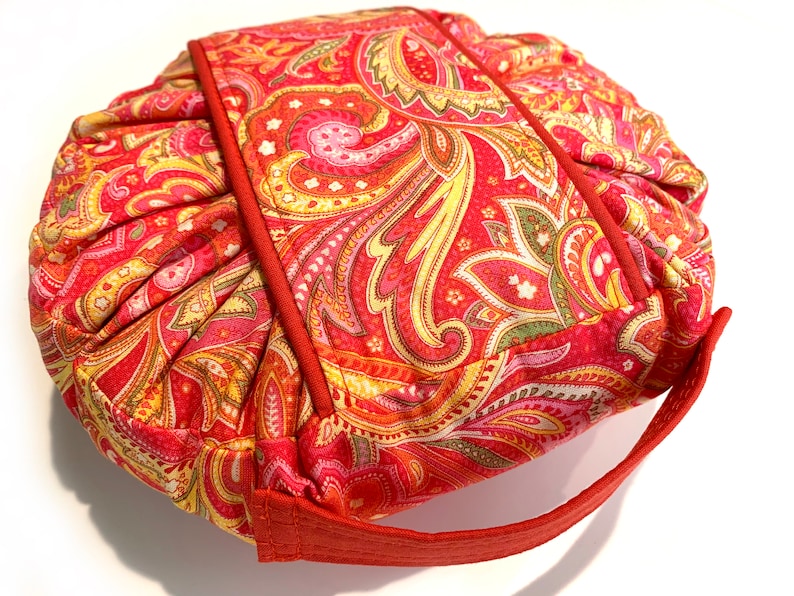 May include: A red, yellow, and green paisley patterned fabric pouch with a red handle.