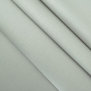 May include: A close-up shot of a light gray fabric with a subtle textured appearance. The fabric is folded in diagonal lines, creating a sense of depth and highlighting the material's drape. The color is a soft, neutral tone.