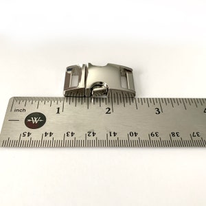 May include: Silver metal slider buckle measuring 1 inch in length. The buckle is shown next to a ruler for size reference.