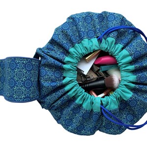 May include: A blue and green drawstring makeup bag with a floral pattern. The bag is open and filled with various makeup items, including brushes, lipsticks, and pencils.