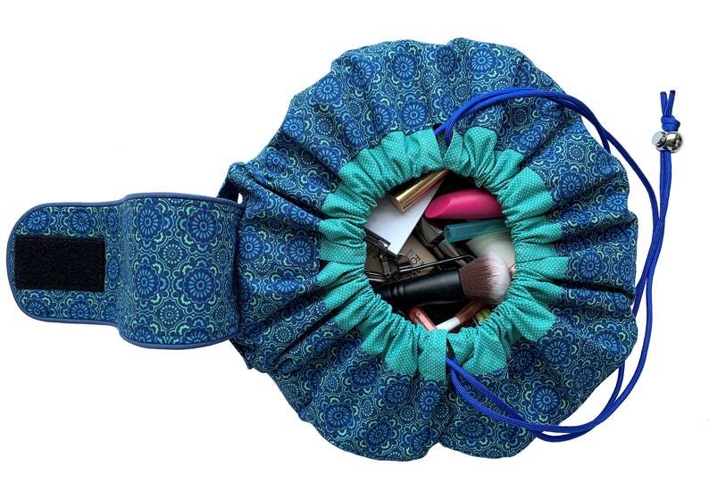 May include: A blue and green drawstring makeup bag with a floral pattern. The bag is open and filled with various makeup items, including brushes, lipsticks, and pencils.