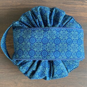 May include: A blue and green fabric drawstring bag with a floral pattern. The bag has a single handle and is gathered at the top.