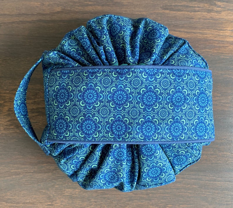 May include: A blue and green fabric drawstring bag with a floral pattern. The bag has a single handle and is gathered at the top.