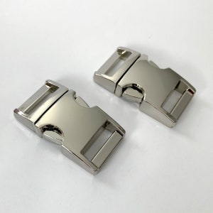 May include: Two silver metal side release buckles. The buckles are rectangular with a smooth, shiny finish.