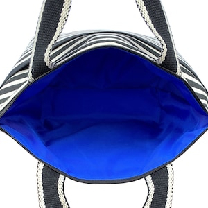 May include: A black and white striped tote bag with black handles and a blue lining. The bag is open and the lining is visible.
