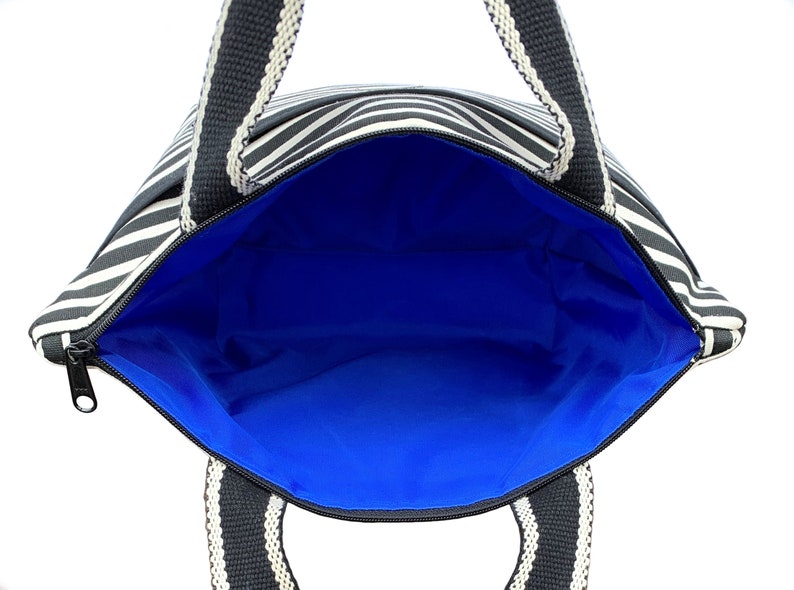 May include: A black and white striped tote bag with black handles and a blue lining. The bag is open and the lining is visible.