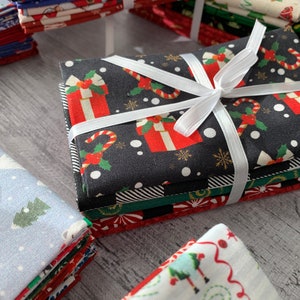 May include: Stacks of Christmas themed fabric squares with various patterns, including snowmen, candy canes, and presents. The fabric is tied with a white ribbon.