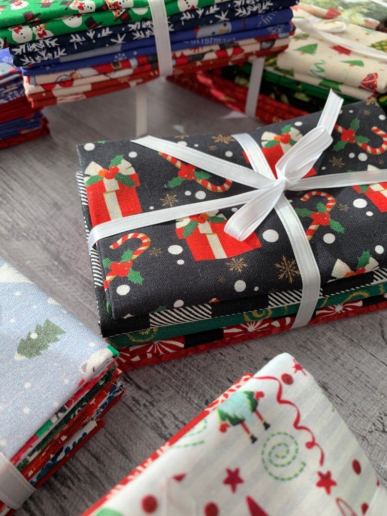 May include: Stacks of Christmas themed fabric squares with various patterns, including snowmen, candy canes, and presents. The fabric is tied with a white ribbon.