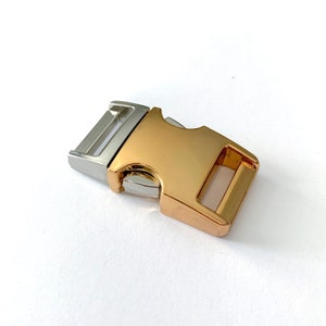May include: A gold and silver metal buckle with a side release clasp. The buckle is designed for use on a dog collar or leash.