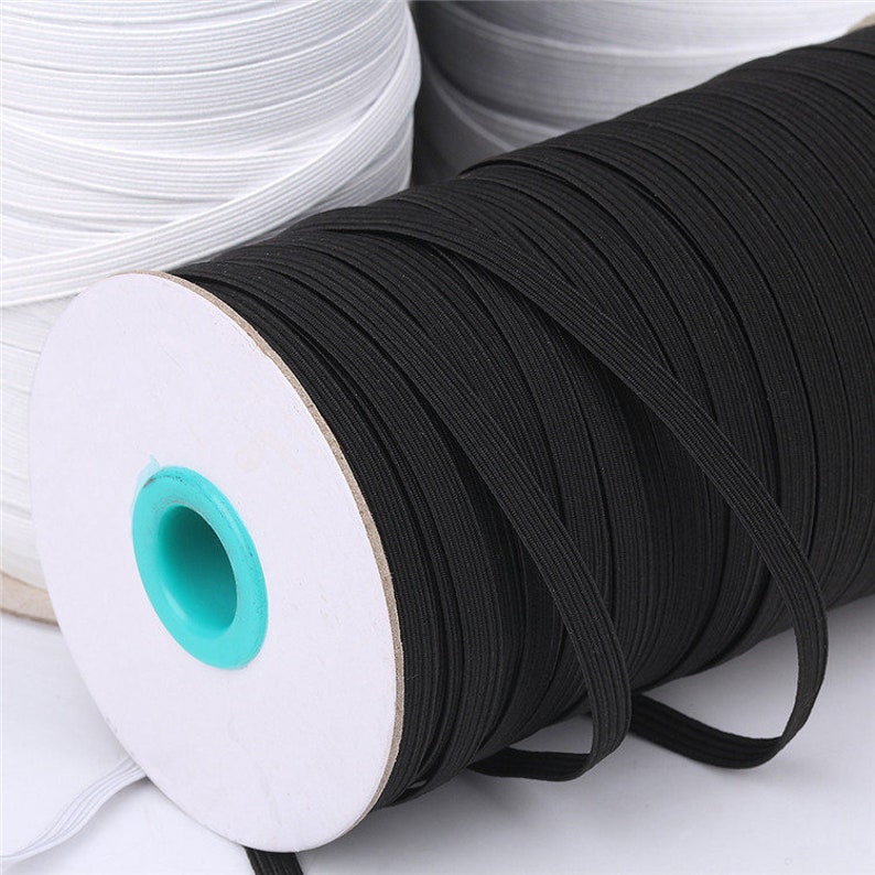 May include: Close-up of a spool of black elastic ribbon. The ribbon is tightly wound around a white cardboard core with a turquoise center. Rolls of white elastic ribbon are visible in the background.