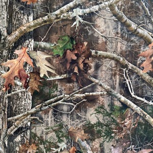 Pode incluir: Padrão de camuflagem com tons de castanho, bege e verde, imitando um ambiente florestal. O design incorpora galhos, folhas e casca, criando uma textura natural. Adequado para roupas e acessórios de exterior.