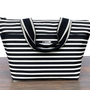 May include: Black and white striped tote bag with black handles and a zipper closure.