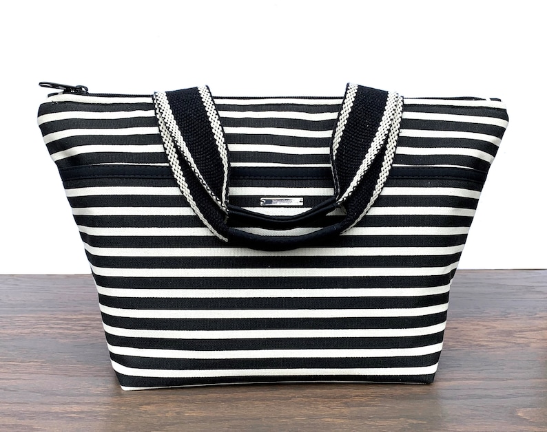 May include: Black and white striped tote bag with black handles and a zipper closure.
