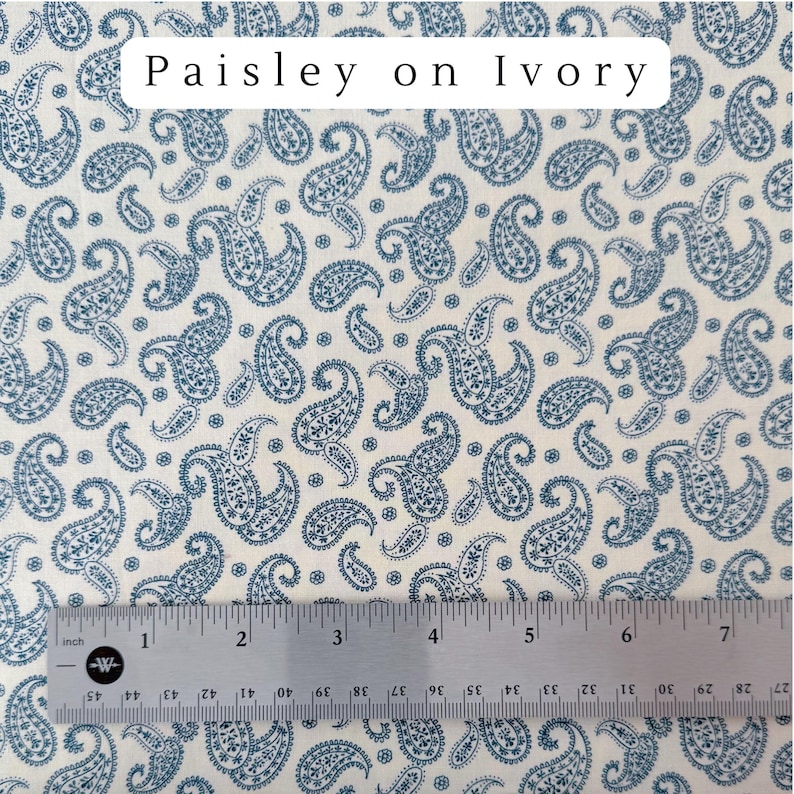May include: Ivory fabric with a blue paisley pattern. The fabric has a repeating design of teardrop-shaped paisley motifs. The text "Paisley on Ivory" is at the top. A ruler is at the bottom, showing inches.