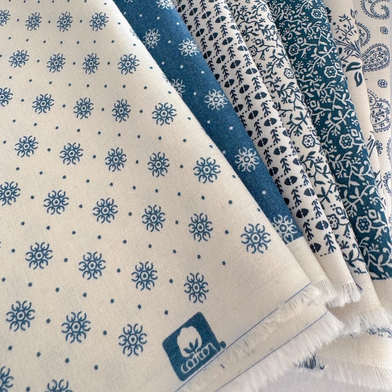 May include: A collection of cotton fabric swatches in various blue and white floral and dotted patterns. The fabrics are folded, revealing the raw edges. A cotton logo is visible on one swatch.