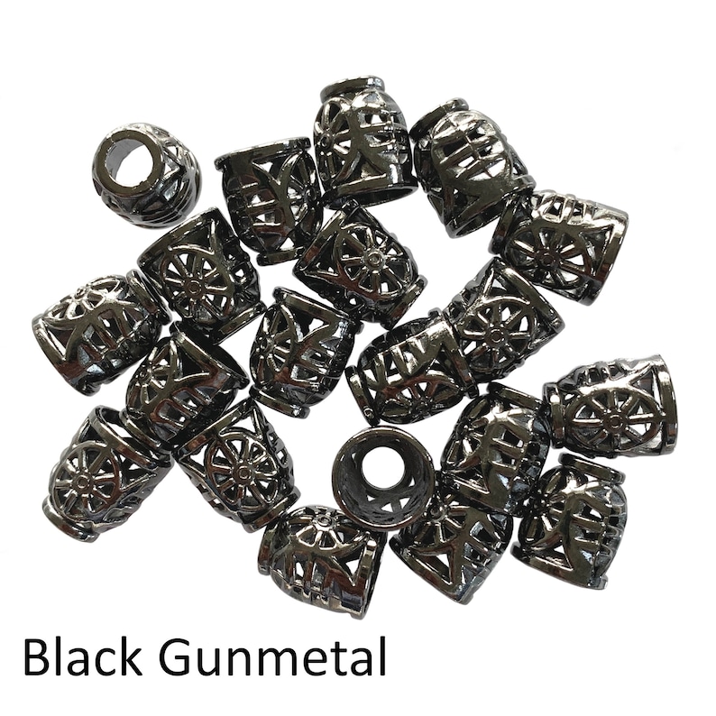 May include: A group of 18 black gunmetal metal beads with a decorative openwork design. The beads are arranged in a pile on a white background.