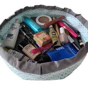 Op de afbeelding: Een grijze en teal trekkoordtas met een stippenpatroon is gevuld met verschillende schoonheids- en hygiëneproducten, waaronder make-up, lotion en zeep.