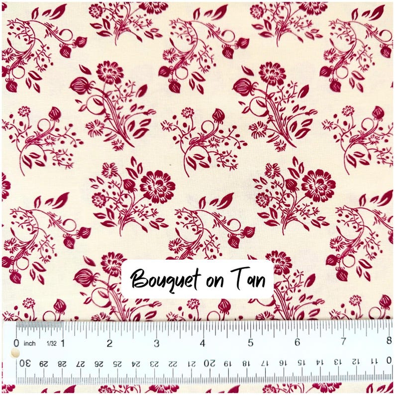 Op de afbeelding: Cr&egrave;mekleurige stof met een herhalend patroon van bordeauxrode bloemboeketten. De boeketten hebben gedetailleerde bloemen, bladeren en stelen. De tekst "Bouquet on Tan" is zichtbaar op de stof.