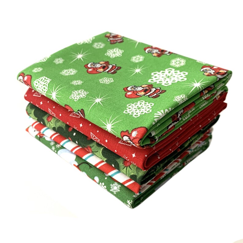 May include: A stack of six green and red Christmas fabric squares with a Santa Claus pattern. The fabric is printed with snowflakes and stars.