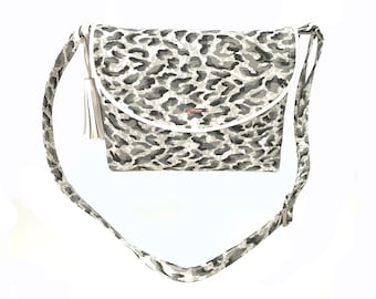 May include: A gray and white leopard print crossbody bag with a white tassel and a silver accent. The bag has a white trim around the edges.