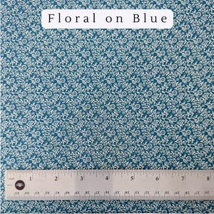May include: Teal fabric with a repeating white floral pattern. The text "Floral on Blue" is at the top. A ruler shows measurements in inches, with a total length of 8 inches.