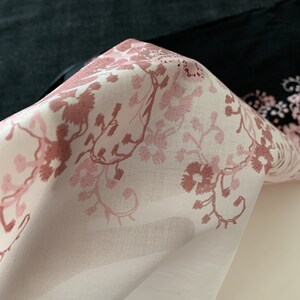 May include: A white fabric with a pink floral pattern. The fabric is folded and the floral pattern is visible on the top layer.