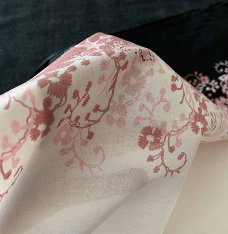 May include: A white fabric with a pink floral pattern. The fabric is folded and the floral pattern is visible on the top layer.