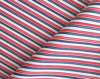 May include: Close-up of a white fabric with a repeating pattern of red and navy blue dotted stripes. The stripes run diagonally across the fabric, creating a textured appearance. The fabric is folded over itself.