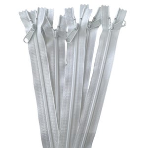 Puede incluir: Una colección de cremalleras blancas, cada una con un tirador a juego. Las cremalleras están dispuestas en forma de abanico, mostrando su longitud y diseño. La imagen está sobre un fondo blanco liso, resaltando los detalles de las cremalleras.