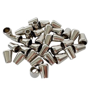 Peut inclure: Un ensemble d'embouts de cordon en métal argenté brillant. Les embouts de cordon ont une forme conique avec un sommet arrondi et un trou pour le cordon. Les objets sont dispersés sur un fond blanc.