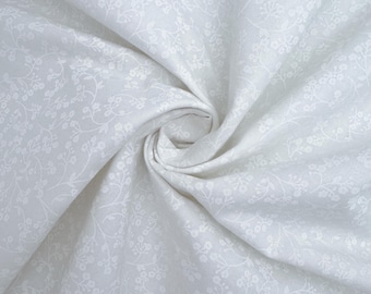 Può includere: Tessuto bianco con un piccolo motivo floreale bianco. Il tessuto è piegato e drappeggiato.