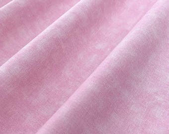 May include: A light pink fabric with a subtle, mottled texture and soft, flowing folds. The material displays a consistent, pale rose hue throughout, characterized by a delicate, cloud-like pattern that creates depth across the surface.